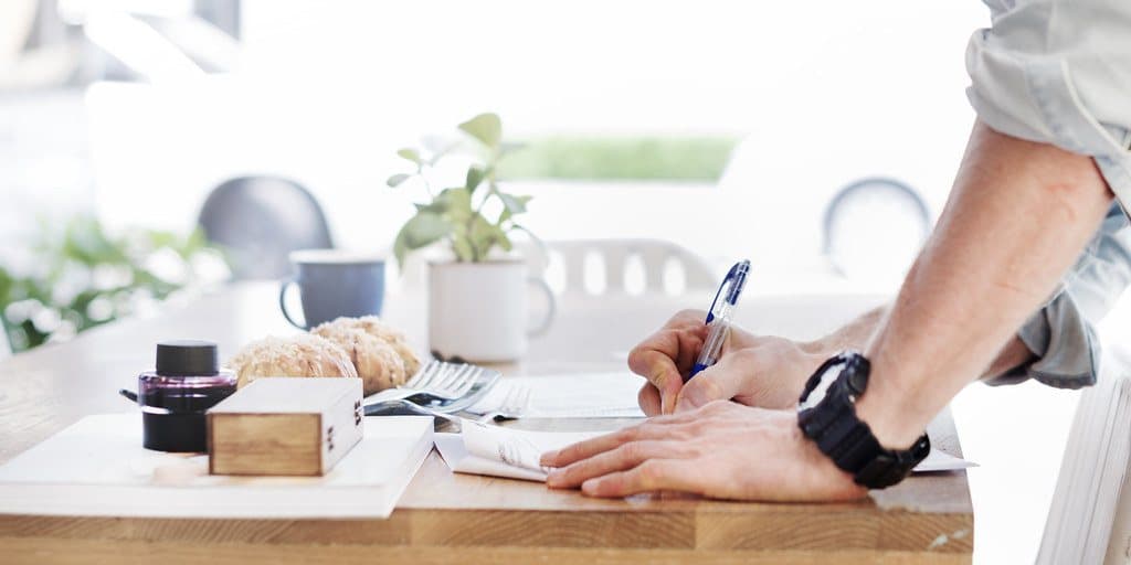 A person completing a printed form at a desk, pen in hand