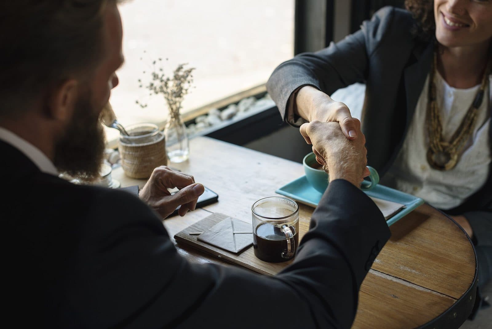 Two people shaking hands across a table where documents and a notebook are laid out