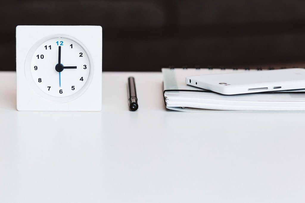 A plain white desk clock beside a notebook and pen