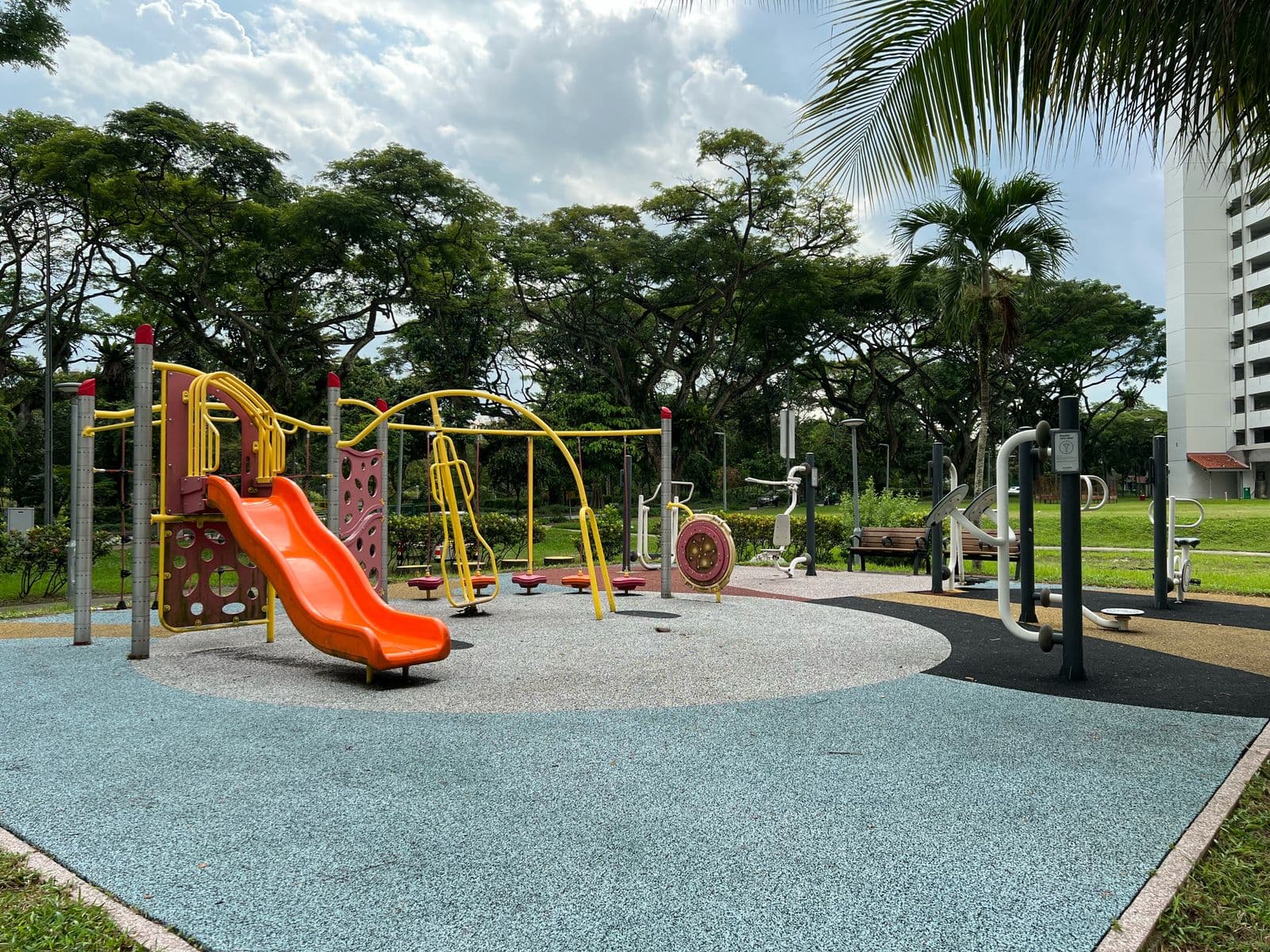 A children's playground with a slide and climbing frame in a Singapore housing estate, palms and an HDB block behind