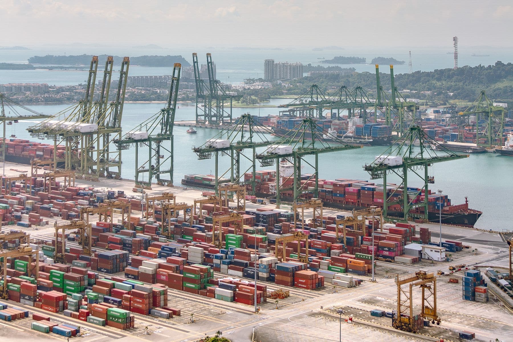 Container cranes and stacked containers at the Port of Singapore, with the strait and islands beyond